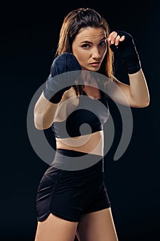 Athletic woman in boxing mittens is practicing karate in studio.