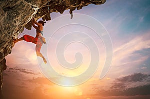 Athletic Woman climbing on overhanging cliff rock with colorful sunset sky background