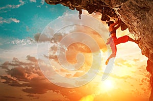 Athletic Woman climbing on overhanging cliff rock with sunset sky background