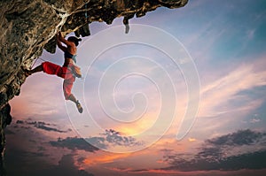 Athletic Woman climbing on overhanging cliff rock with sunset sky background