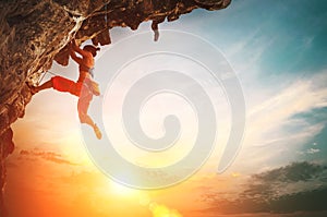 Athletic Woman climbing on overhanging cliff rock with sunset sky background