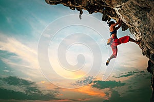 Athletic Woman climbing on overhanging cliff rock with sunset sky background photo