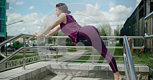 Athletic woman does leaning stretching exercises at the handrails in the yard of an apartment living complex, fitness in