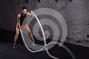 Athletic woman doing battle rope exercises at gym