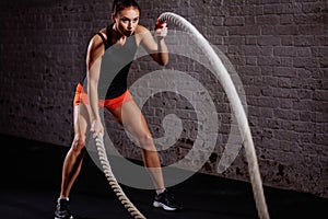 Athletic woman doing battle rope exercises at gym