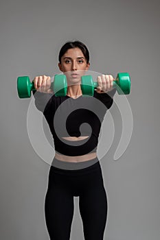 Athletic woman doing dumbbell front raise with both hands on grey background