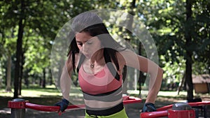 Athletic woman doing push-ups on the uneven bars outdoors