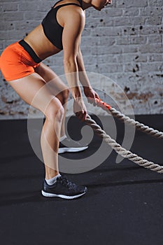 Athletic woman doing some cross fit exercises with battle rope indoor