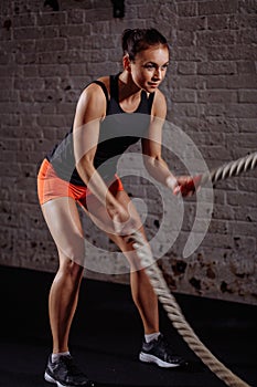 Athletic woman doing some cross fit exercises with battle rope indoor