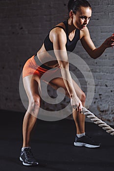 Athletic woman doing some cross fit exercises with battle rope indoor