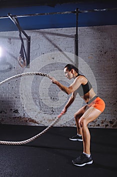 Athletic woman doing some cross fit exercises with battle rope indoor