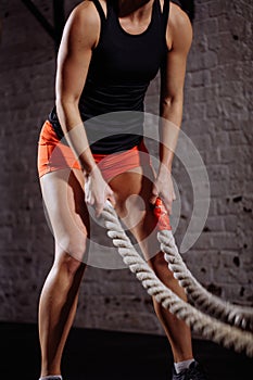 Athletic woman doing some cross fit exercises with battle rope indoor