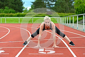 Athletic woman doing straddle stretches on track photo
