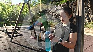 Athletic woman drinking water from bottle, relaxing after workout set outdoors