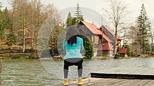 athletic woman in leggings crouches on the shore of a mountain lake in norway