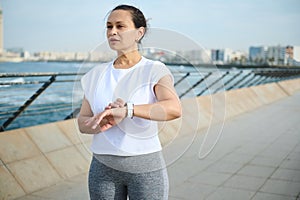 Athletic woman looking into the distance, checking fitness application on smartwatch, getting ready for morning jog
