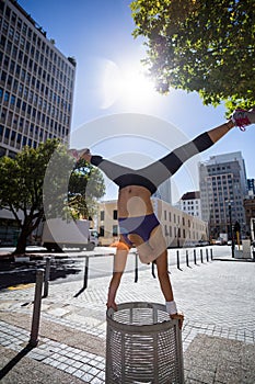 Athletic woman performing handstand and doing split on bin