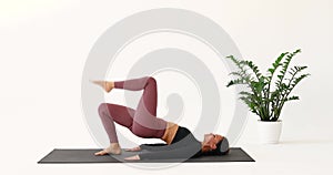An athletic woman performs the Dvipada Pithasana exercise, a half-bridge pose with alternate lifting of the legs upward