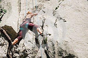 Athletic Woman in protective helmet and shoes climbing on cliff rock wall using top rope and climbing harness in Paklenica