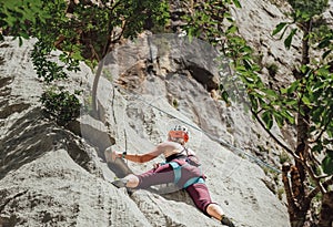 Athletic Woman in protective helmet and shoes climbing on cliff rock wall using top rope and climbing harness in Paklenica