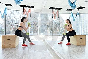 Athletic woman pumping up muscles with dumbbells before workday at fitness gym