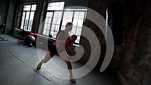 Athletic woman is punching box bag in gym, practicing hands punches