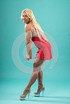 Athletic woman in red dress posing in studio. Attractive fitness lady with long blond hair showing her muscles.
