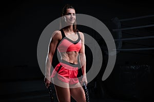 Athletic woman in red shorts and top exercising with ropes in functional training area. Fitness concept