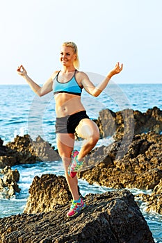 Athletic woman relaxing - practicing yoga on the rocks by the se