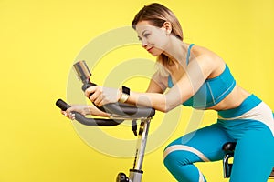 Athletic woman riding exercise bike and looking tutorial video on smart phone, cardio workout.