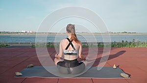 Athletic Woman Sitting in lotus position and Doing Yoga Lake Background. Beautiful Girl Exercising Outdoors. Stretching Exercises