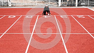 Athletic woman in sport clothes on starting line prepares to run at the running on athletic track. Female runner ready for sports