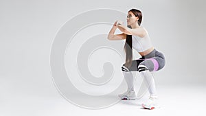 Athletic woman in sports wear squatting with resistance band at studio. Fitness model doing squat exercise