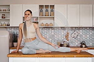 Athletic woman in sportswear posing on the table top of a light modern kitchen