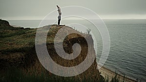 Athletic woman stand straightening up beach hill stretch hands to gray sky.