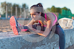 Athletic woman stretching her hamstring, legs exercise training fitness before workout outside on a beach at summer