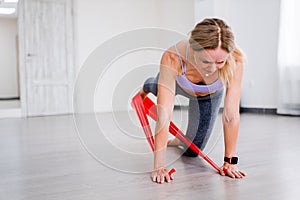 Athletic woman swings her leg back using red resistance band, kickback exercise of Pilates close up