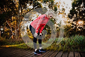 Athletic woman tired from run in the park, bent over breathing heavily