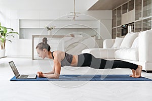 Athletic woman training at home using laptop