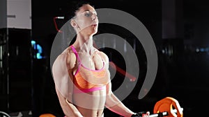 Athletic woman trains muscles of the hands with a barbell.