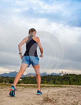 Athletic woman warming up before her morning workout in the forest mountain road. Runner training outdoors, healthy