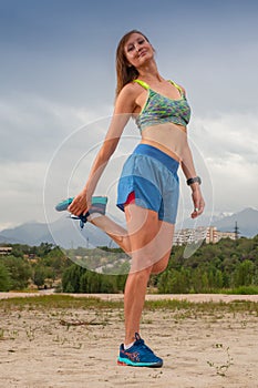 Athletic woman warming up before her morning workout in the forest mountain road. Runner training outdoors, healthy