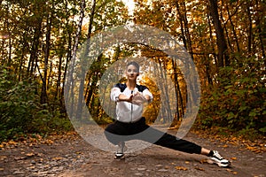 Athletic woman warms up in park before jogging. Healthy lifestyle concept. Sporty woman with hair in ponytail stretching