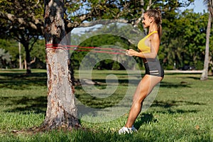 Athletic woman workout with resistance band outdoors. Fitness girl doing exercise for back at the park