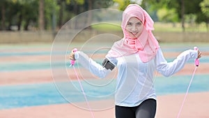 Athletic young asian muslim woman in sportswear standing and skipping rope outdoor for morning exercise. Active girl work out on