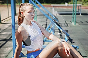 Athletic young blond woman sits and rests on sports field during her vacation from workouts