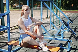Athletic young blond woman sits and rests on sports field during her vacation from workouts