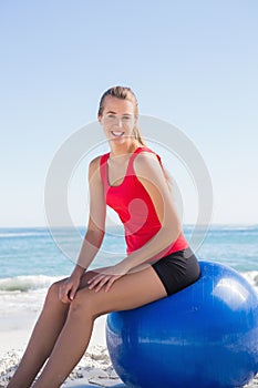 Athletic young blonde sitting on exercise ball looking at camera