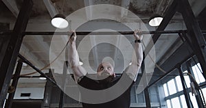 Athletic young Caucasian man doing pull-up exercises during functional workout in large atmospheric gym slow motion.