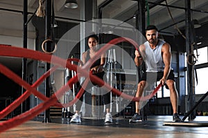 Athletic young couple with battle rope doing exercise in functional training fitness gym